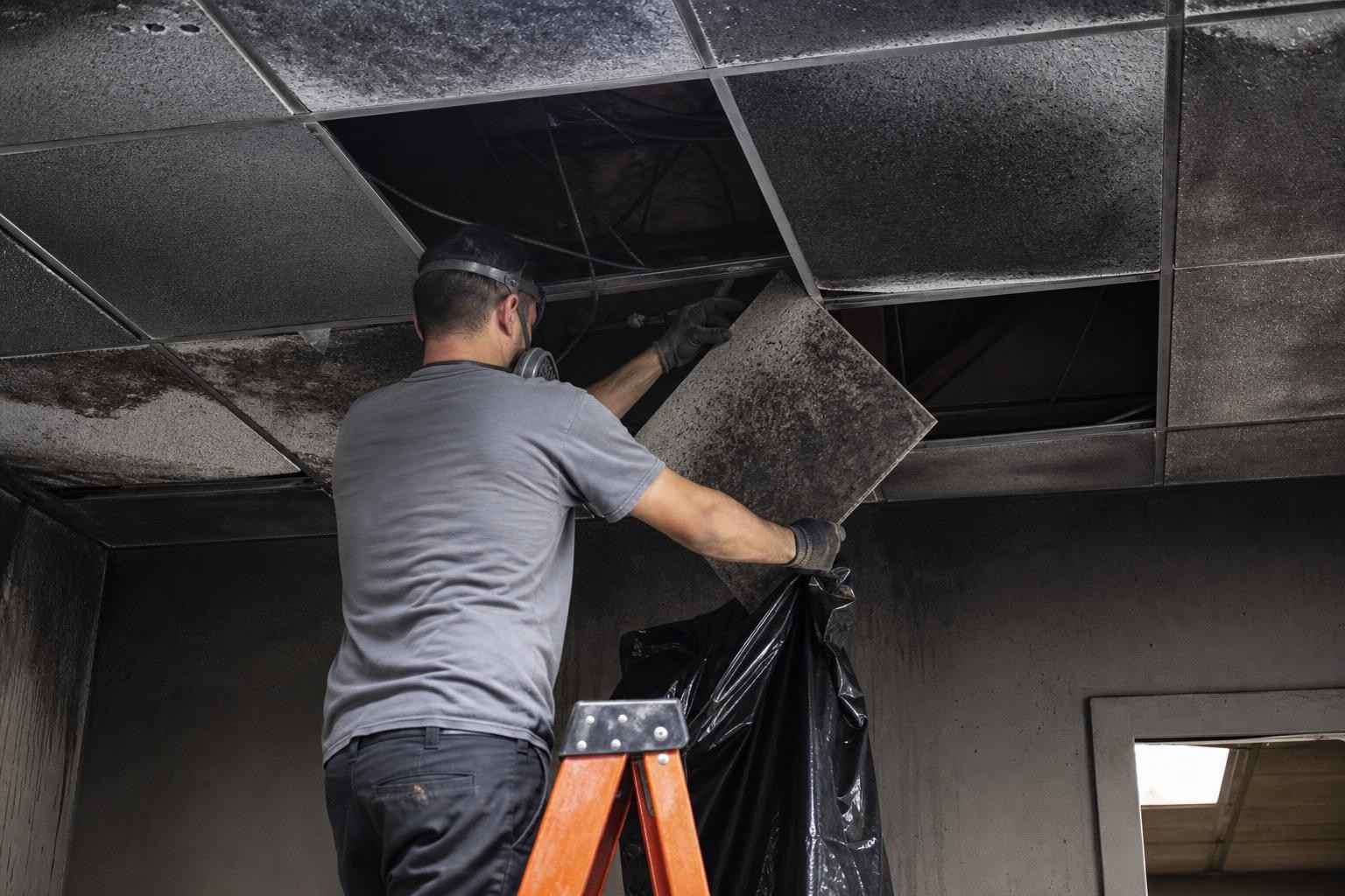 Technician removing fire-damaged ceiling tiles in a commercial building in Dallas TX