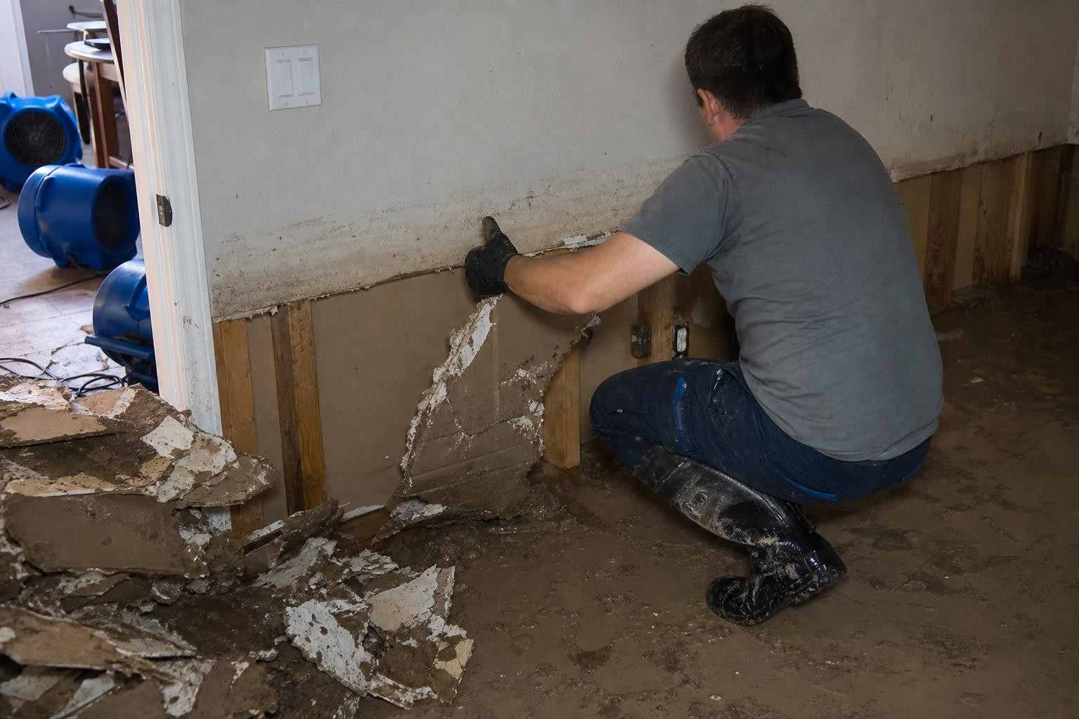 Technician removing flood-damaged drywall during flood restoration in a Dallas TX home