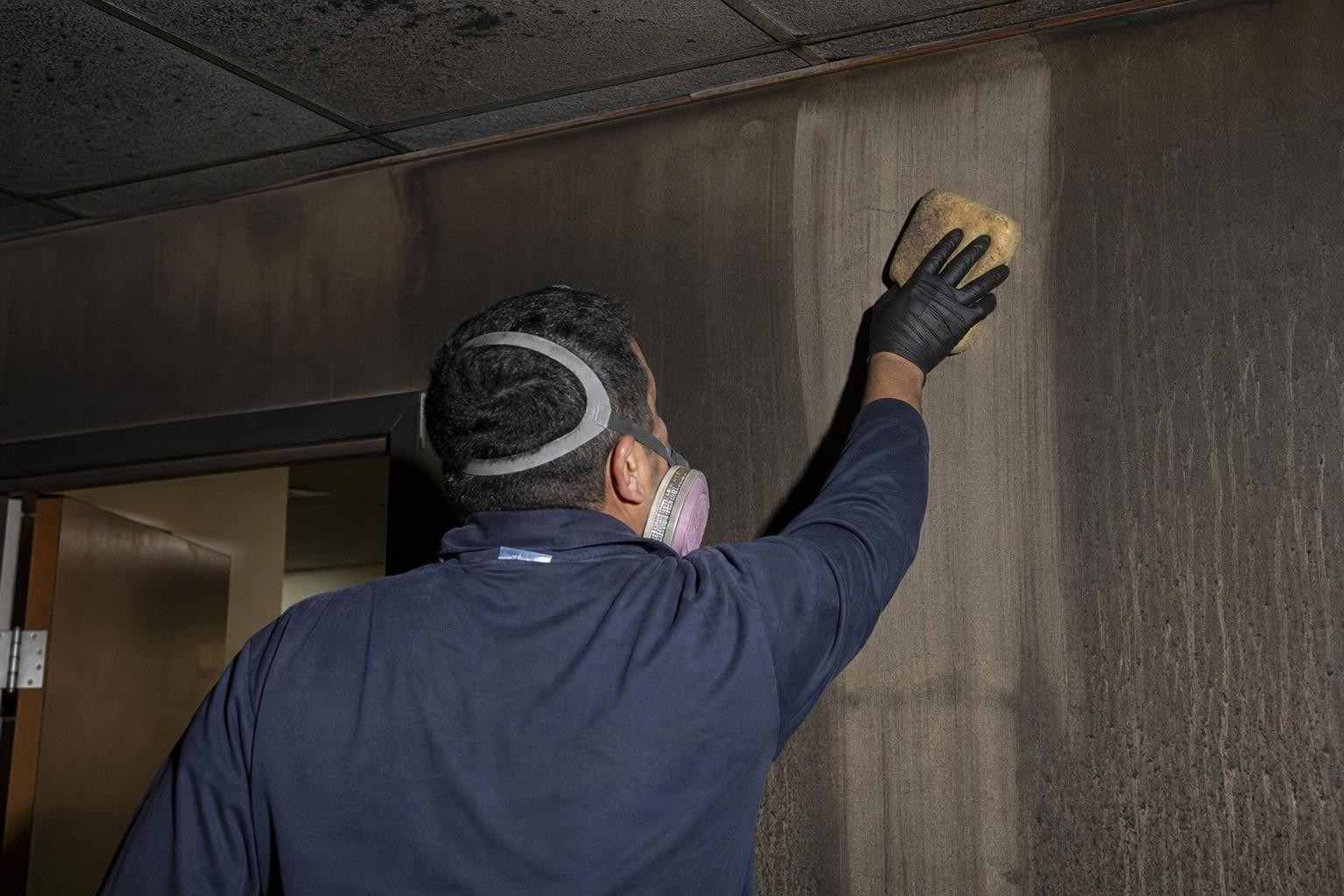 Technician wiping heavy soot off a wall during smoke and soot damage cleanup in Dallas TX